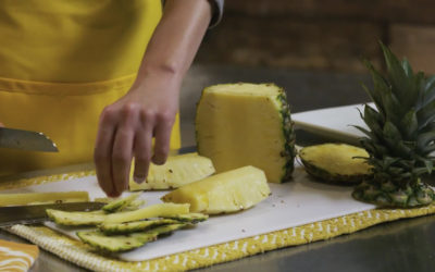 A produce clerk cuts up a pineapple