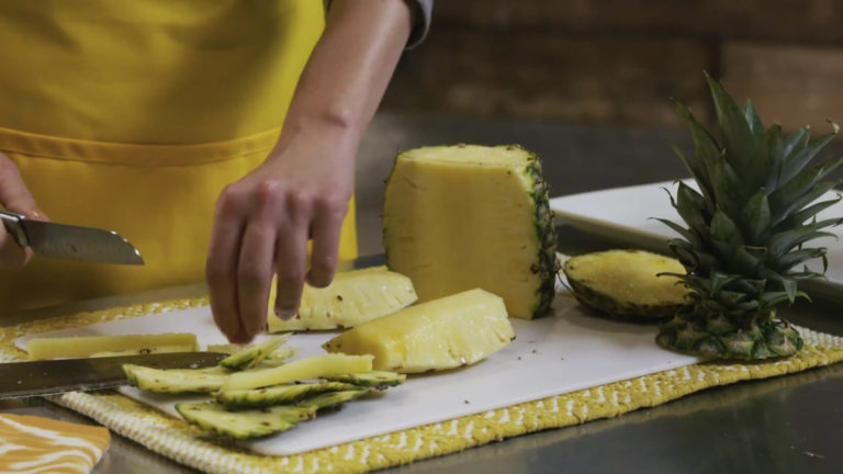 A produce clerk cuts up a pineapple
