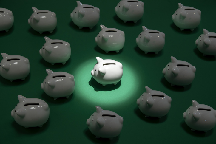 many small white piggy banks on green surface one piggy bank being spot lit