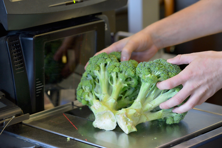 Close up of a person weighing broccoli at a self check out counter at a supermarket