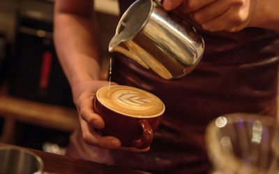 A barista pours hot milk foam to create latte art in a mug