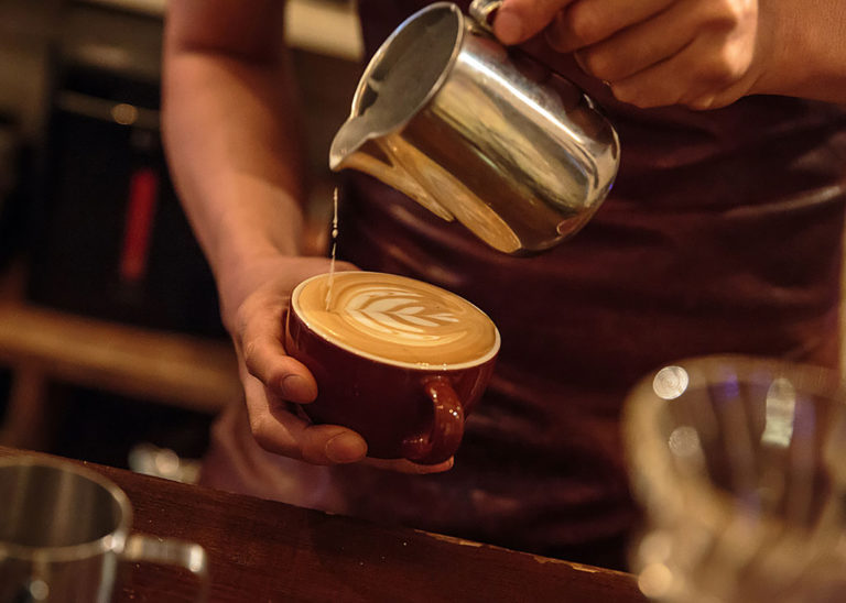 A barista pours hot milk foam to create latte art in a mug