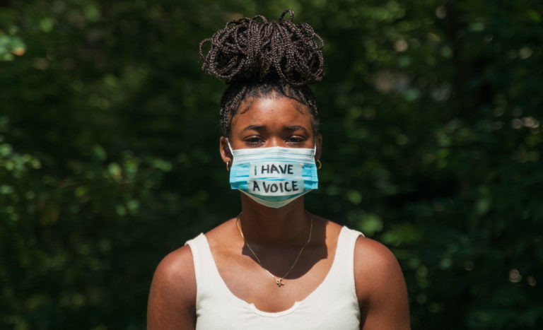 A young Black woman wears a face mask during global pandemic that says 