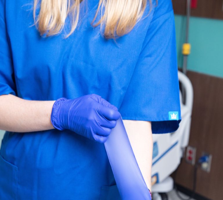 Closeup of a nurse putting on a pair of blue gloves next to a patient's bed