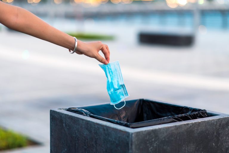 Woman throwing used protective surgical mask into the garbage bin